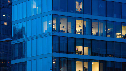 Illuminated Offices in a Modern Blue Glass Building at Twilight with People Working Late ©  Blar Studio
