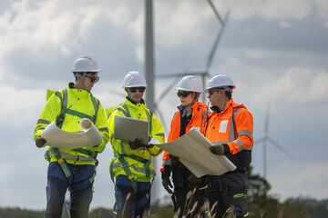 Fototapeta premium Engineers reviewing blueprints at wind farm, illustrating teamwork, safety and the advancement of clean renewable energy through professional field planning and technical collaboration.