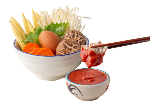 chopsticks picked pork dipped into a bowl of sukiyaki sauce, Many vegetables in white bowl include carrots, baby corn, shiitake mushrooms, golden needles, celery and chicken eggs.