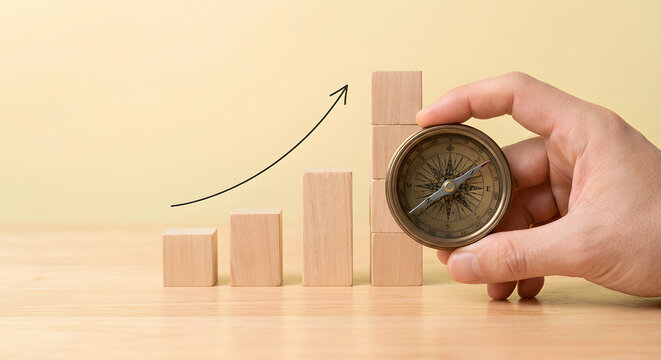 hand holding vintage brass compass next to ascending wooden blocks with rising arrow for business direction strategy financial growth career path and navigation to success concept