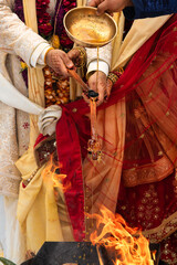 Groom Offering Ghee During Traditional Hindu Vivaha Homa Ceremony, sacred ghee from a brass bowl