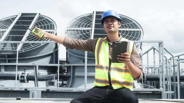 Two construction engineers in safety gear examine industrial HVAC units on rooftop, pointing and discussing project progress and setup.