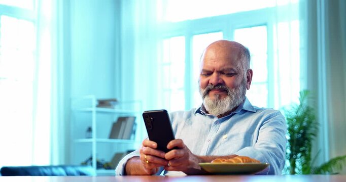 Indian young son serving black tea or coffee to senior father sitting at table in the morning at home, caring family moment as elderly parent tastes drink and happily approves flavor with warm smile