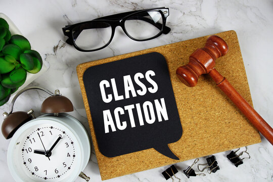 Class Action text on speech bubble with alarm clock and wooden gavel on marble background