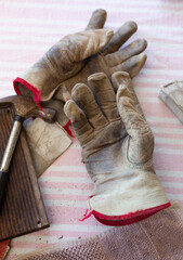 Still life of leather work gloves with small hammer and pieces of worn sandpaper