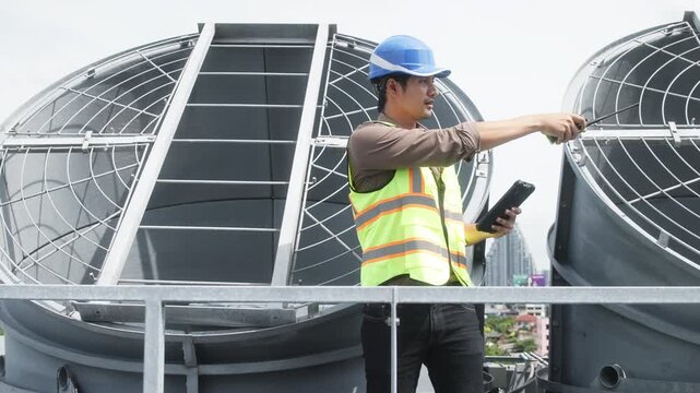 Two construction engineers in safety gear examine industrial HVAC units on rooftop, pointing and discussing project progress and setup.