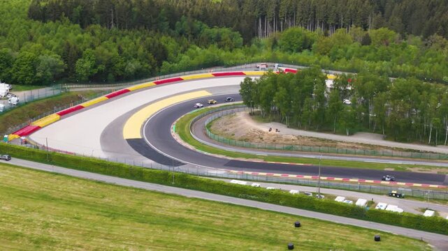race cars navigate pouhon corner spa francorchamps grey runoff yellow red safety barriers belgian forest background wide spa-francorchamps belgium multiple 