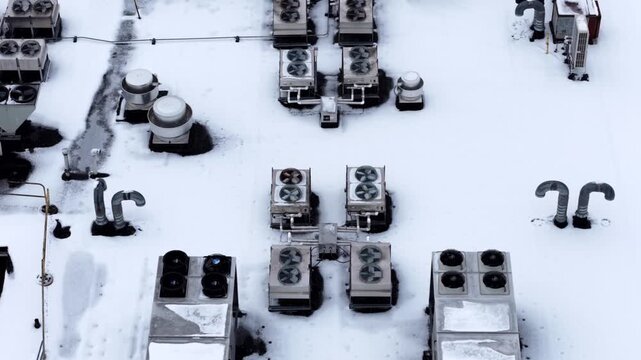 Commercial building roof covered in snow in the United States. Industrial ventilation systems and HVAC units during winter. Aerial top down shot.