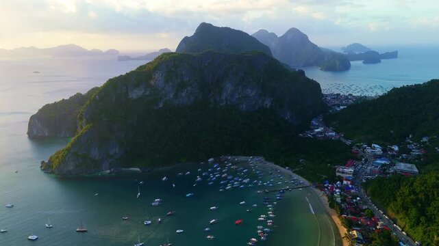Cinematic aerial view of El Nido bay and limestone cliffs in Palawan, Philippines. High-angle shot of outrigger boats and the town at dusk. Scenic tropical nature landscape