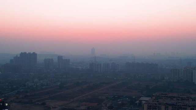 Hazy sunset view over Gurgaon cityscape with high-rise buildings fading into smog, highlighting urban pollution, atmospheric haze, and metropolitan landscape.