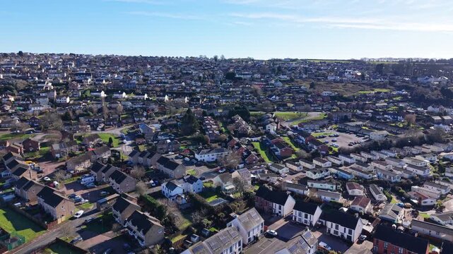 Drone aerial footage of Cinderford town in Gloucestershire, surrounded by the Forest of Dean, showing residential buildings, townscape, woodland, and rolling hills in a semi-urban rural landscape