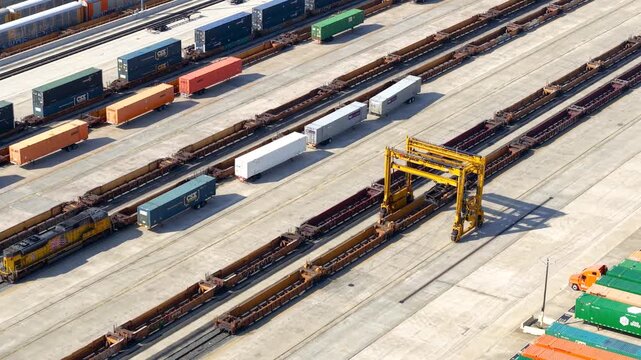 Aerial view of a yellow gantry crane moving along freight trains and shipping containers