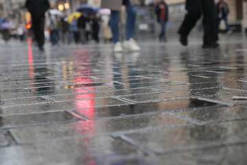 Fototapeta premium People walk on wet pavement in the city during rain