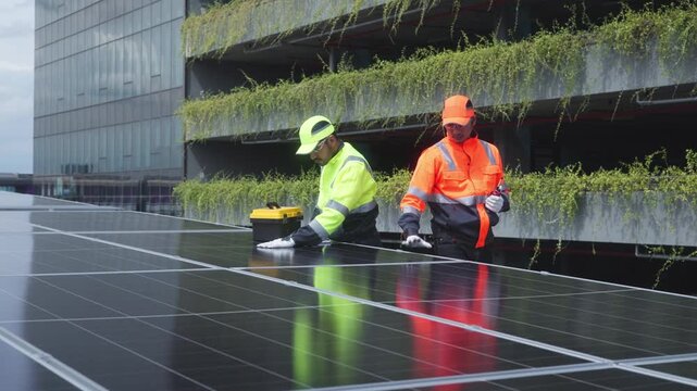 Two technicians in high-visibility uniforms examine and align solar panels on a rooftop, using blueprints and tools for proper setup.