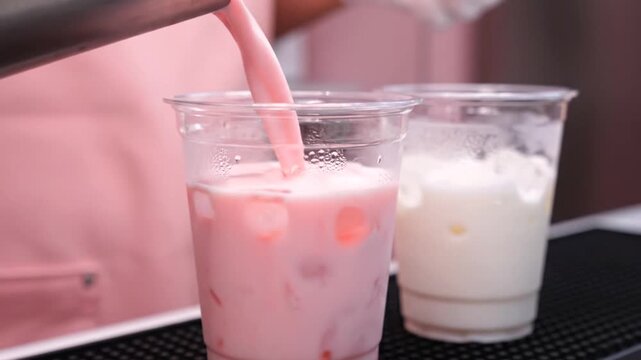 A captivating moment as a colorful pink drink, full of refreshing flavor, is carefully poured into a clear cup with ice, promising a delightful sweet treat