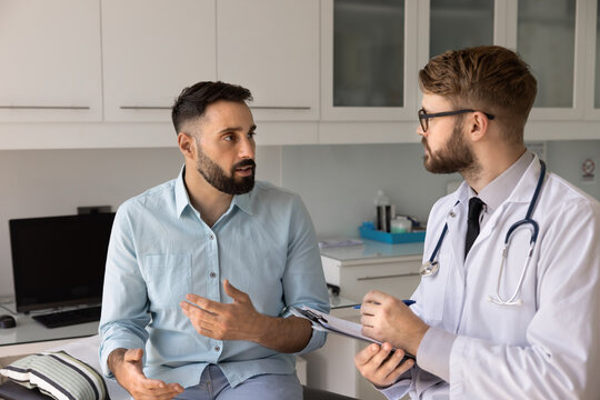 On trusted doctor appointment. Young male patient visit hospital for medical checkup sit on couch in examination room talk share concerns with gp explain health issues complaints during consultation