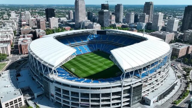 Aerial view of a large soccer stadium in a city with blue seats and green field 4k video
