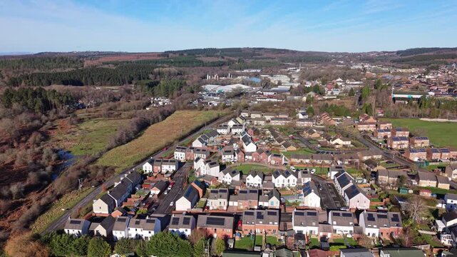 Drone aerial footage of Cinderford town in Gloucestershire, surrounded by the Forest of Dean, showing residential buildings, townscape, woodland, and rolling hills in a semi-urban rural landscape