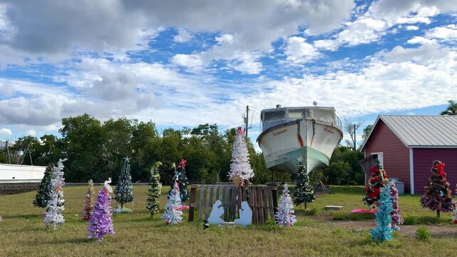 Outdoor Christmas display in Cape Coral, Florida featuring a traditional nativity scene, various decorated Christmas trees, and a boat set against a cloudy sky during the holiday season