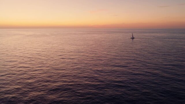 Scenic footage of a sailboat sailing solo on the horizon at dawn. Aerial