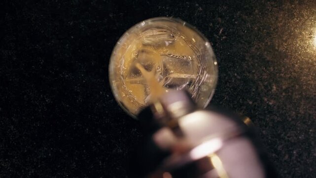Alcoholic drink being poured over crystal-clear ice cubes in a cocktail glass against a dark background.