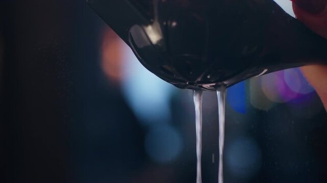 Close up of lime juice squirting from hand press into cocktail glass in bar lighting.
