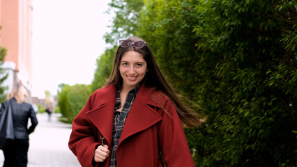 Portrait photo of happy young smiling woman in burgundy coat during city walk outdoors