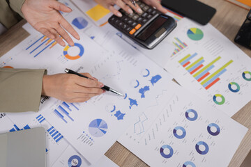 Top view of business people analyzing marketing reports, financial charts, and sales performance using calculators and pens in a meeting room.