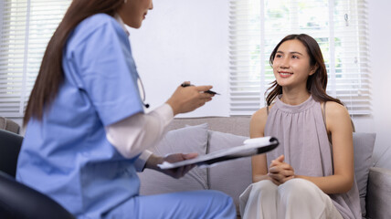 Obraz premium Young female doctor or nurse in blue scrubs consulting with a female patient at home, discussing chest X-ray results and giving healthcare advice during a home visit service.
