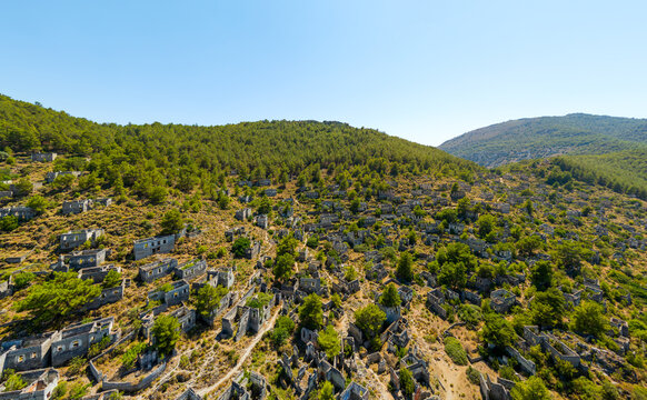 Kayakoy, Turkey. Aerial view of decaying stone architecture in Levissi ghost town on mountain slope, showing crumbling walls and roofless houses surrounded by forest. Aerial view