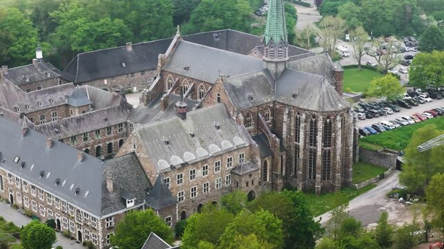 massive buttresses copper spire dominate eastern elevation above slate roofs activity below adds scale val dieu abbey belgium val-dieu human architectural weight 