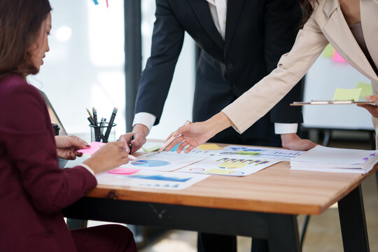 A dynamic office setting where a group of business professionals are having a productive meeting. The desk is covered with data analysis reports and colorful sticky notes, as team members engage in a 