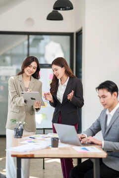 Group of young Asian professionals engaging in a dynamic brainstorming session. A female leader stands confidently while presenting ideas to her colleagues, showcasing a collaborative, positive