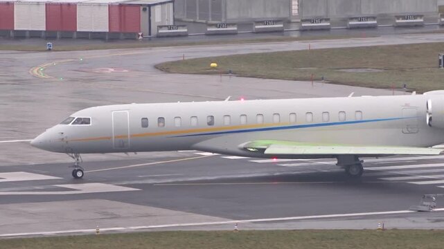 private jet plain white livery blue yellow stripes taxiing wet runway markings zurich airport under misty overcast and conditions regional 