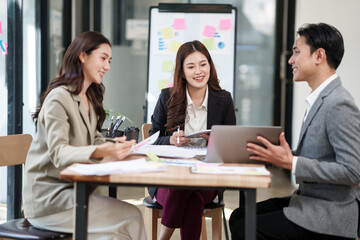 Obraz premium Group of young Asian professionals engaging in a dynamic brainstorming session. A female leader stands confidently while presenting ideas to her colleagues, showcasing a collaborative, positive