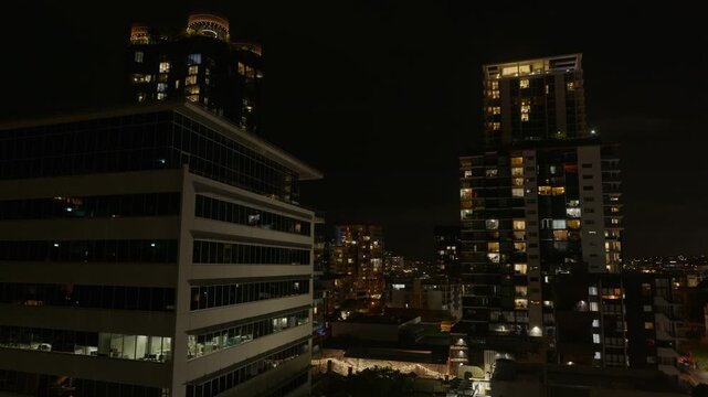 Pan Right, Brisbane city buildings and high rises at night time with lights from rooms illuminated.