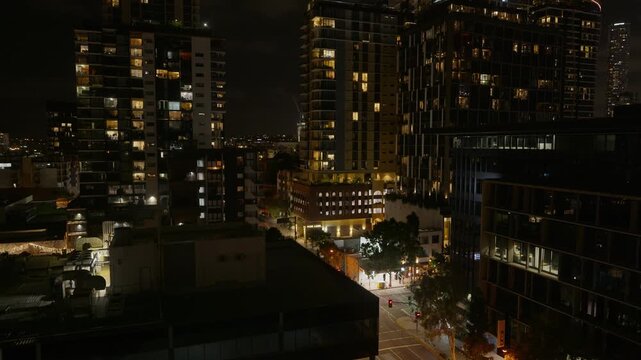 Tilt down, A busy street in Brisbane City lit up with cars driving and stopping at traffic lights with buildings and high rises in the background.