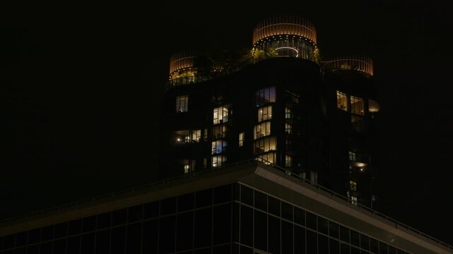 Pan right, The rooftop of a high rise at night time with lights and roof top garden illuminated.