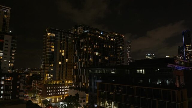 Pan Left, The city scape of Brisbane at night time with illuminated high rise apartment buildings and shops.