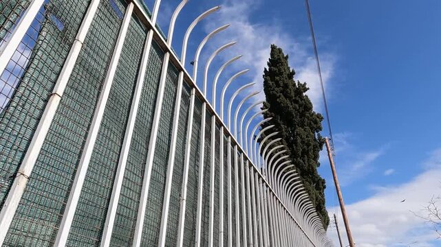 Trucking camera movement from low angle  follows a wall with tall curved white metal railings