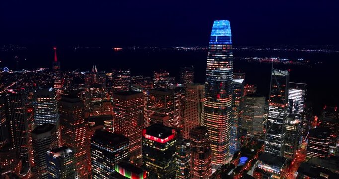 Outstanding scenery of San Francisco downtown, California, USA at night. Approaching the blue neon top of the Salesforce Tower in the midtown. Dark waterscape of the bay at backdrop.