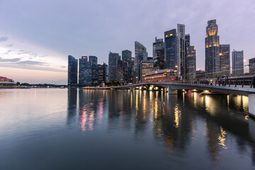 Obraz premium Sinpapore: The lights of the skyscrapers of Singapore business district reflect on the water of the Marina bay in Singapore during sunset.