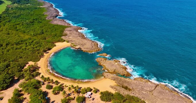 Panoramic aerial view of Mar Chiquita beach and cliffs. Wide drone perspective of a rocky coastline, natural pool, and dense tropical forest under bright sun.