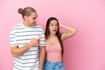 Naklejka premium Young caucasian couple isolated on pink background pointing finger to the side with a surprised face