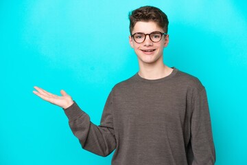 Fototapeta premium Teenager Russian man isolated on blue background holding copyspace imaginary on the palm to insert an ad