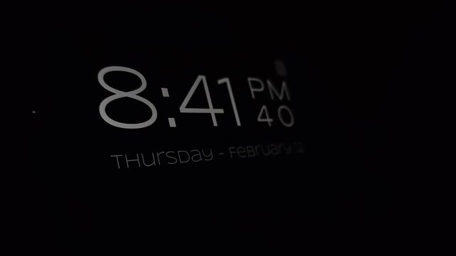 Close-up of a smartphone on a metal stand displaying a digital clock at 8:41 PM, with warm ambient background light turning off and leaving the screen glowing in the dark, bedside nightstand concept.