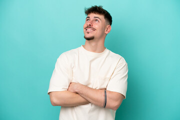 Fototapeta premium Young caucasian handsome man isolated on blue background looking up while smiling