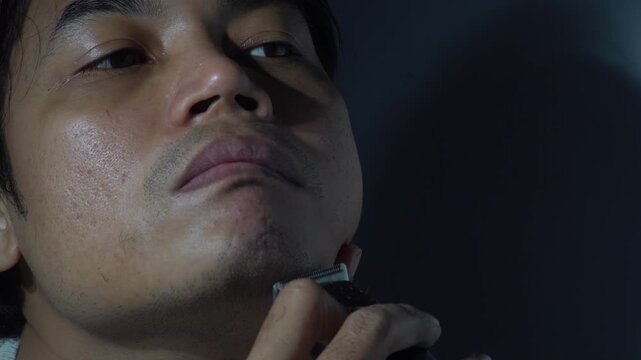 Close-up of an Asian man using an electric trimmer to shave his chin. The video highlights skin texture, facial hair removal, and daily morning grooming routine with authentic lighting. Perfect for ma