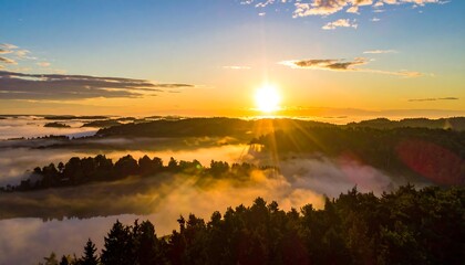 Obraz premium Aerial view of a radiant sunrise over forested hills and a misty valley, with a lake reflecting the golden light