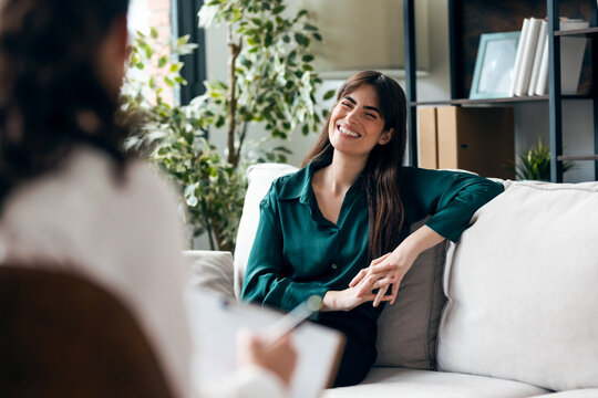 Beautiful woman having therapy while the psychologist takes notes, sitting on the couch in the psychology office